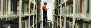 Eine Studentin steht zwischen zwei Bücherregalen in einer Bibliothek